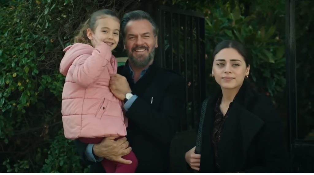 Kadr z 364. odcinka serialu "Dziedzictwo". Fikret stoi przed domem, trzymając Melek na rękach. Dziewczynka radośnie macha do odjeżdżających Yusufa i Yamana, a na twarzy Fikreta widać dumę i radość z chwil spędzonych z córką. Obok Fikreta stoi Seher, także się uśmiechając. Atmosfera jest pełna ciepła i rodzinnej więzi.