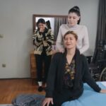 Canan siedzi na łóżku Zuhal, a Cicek robi jej masaż. Zuhal stoi, opierając się o komodę.