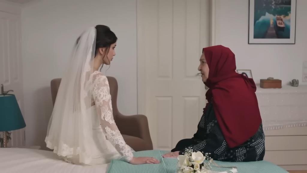Duygu ubrana jest w piękną suknię ślubną, a w jej włosach delikatnie spoczywa welon. Ona i Sultan siedzą razem na łóżku.