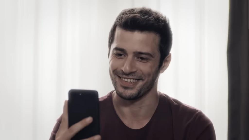 Aziz uśmiecha się, trzymając w ręku telefon.