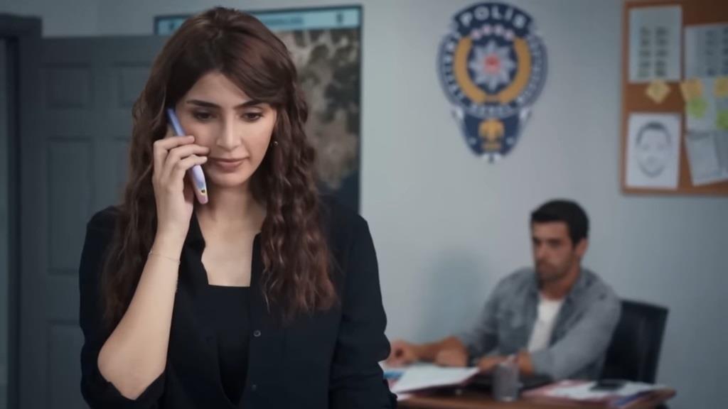 Duygu rozmawia przez telefon. Siedzący za biurkiem Ali obserwuje ją uważnie.