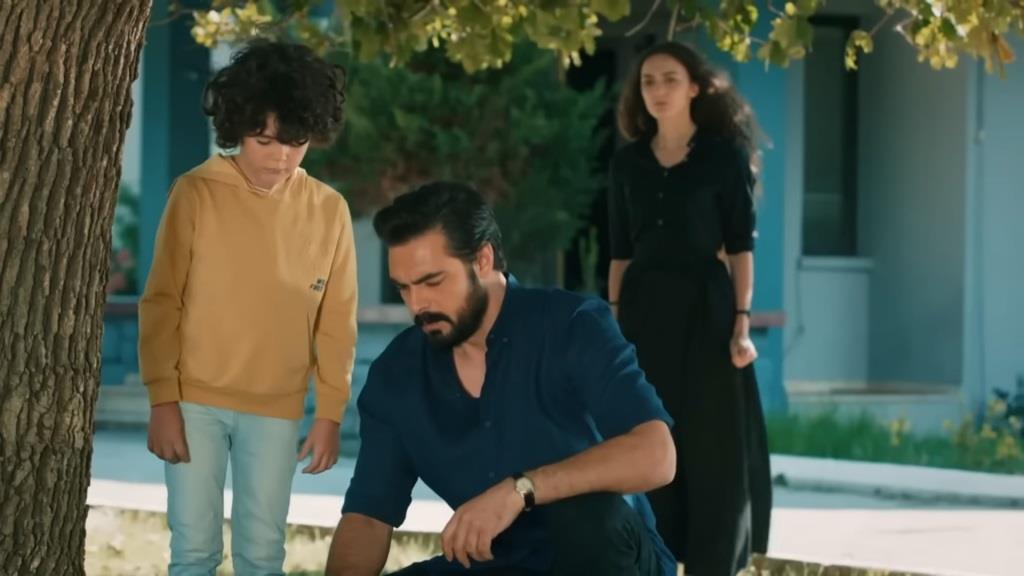 Yusuf stoi przy drzewie, a Yaman kuca obok niego. Za nimi znajduje się Nana.