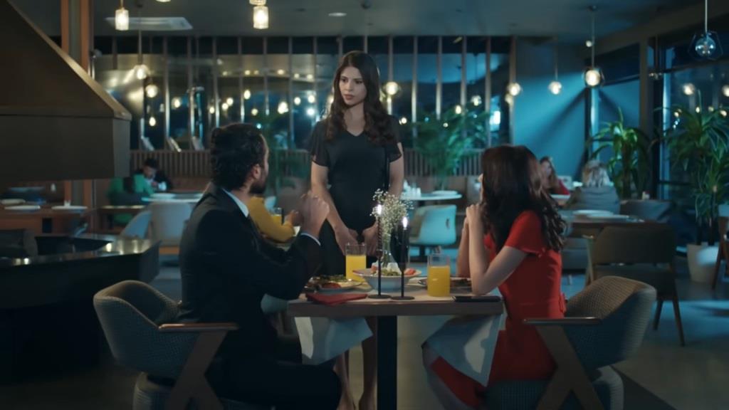 Ferit siedzi wraz z Nalan przy stoliku w hotelowej restauracji. Ayse stoi obok nich.