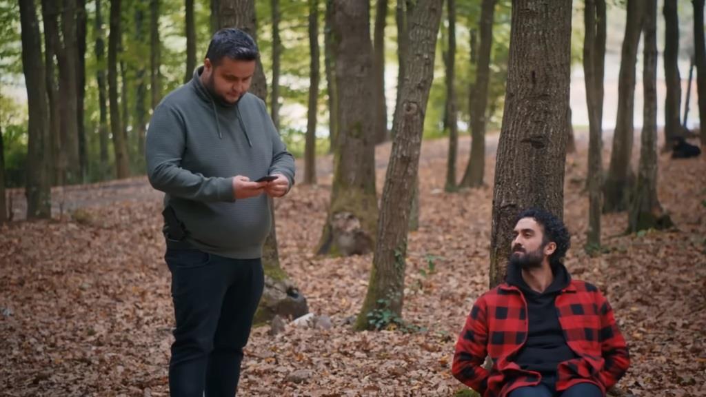 Ferit jest przywiązany do drzewa w lesie. Obok stoi zbir.