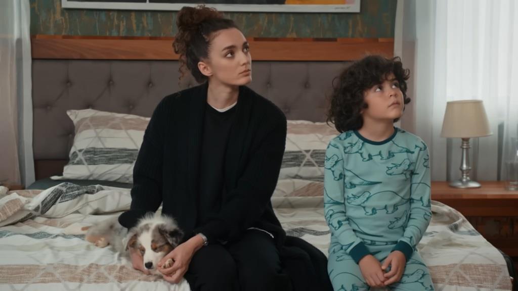 Yusuf i Nana siedzą na łóżku, wpatrzeni w jeden punkt. Nana trzyma w rękach szczeniaka.