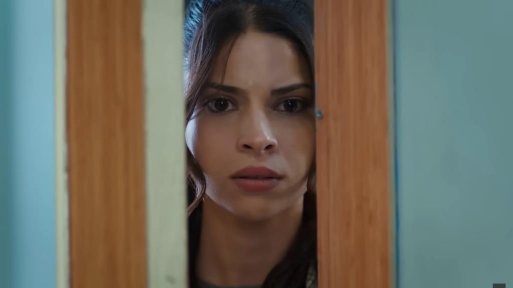 Ayse stoi przy uchylonych drzwiach sali szpitalnej.