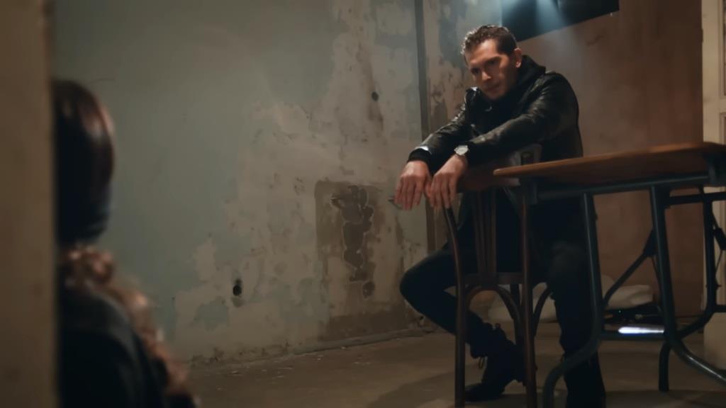 Ertan siedzi na odwróconym krześle i patrzy na Ayse - swoją zakładniczkę.