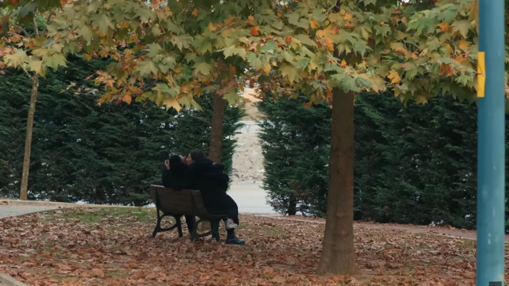 Widok na ławkę w parku, na której siedzą Pelin i Ferit. Dziewczyna całuje mężczyznę.