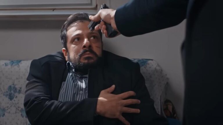 Idris spogląda w wycelowaną w siebie lufę pistoletu.