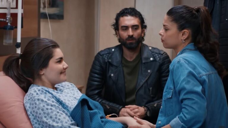 Nese uśmiecha się. Ayse siedzi przy niej, trzymając jej rękę. Ferit siedzi między nimi.