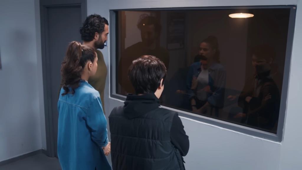 Kara, Ayse i Ferit zaglądają przez szybę do pokoju przesłuchań.