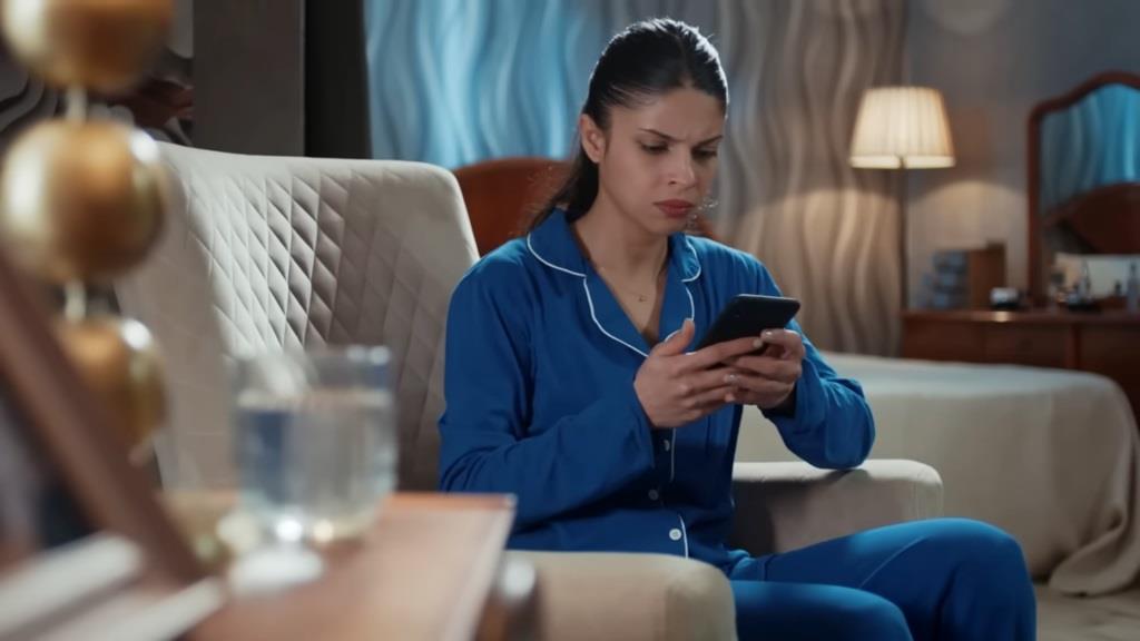 Ayse, ubrana w piżamę, odczytuje wiadomość na telefonie.