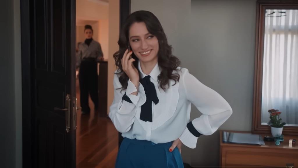 Hazal rozmawia przez telefon, uśmiechnięta od ucha do ucha, a Nana obserwuje ją z korytarza.