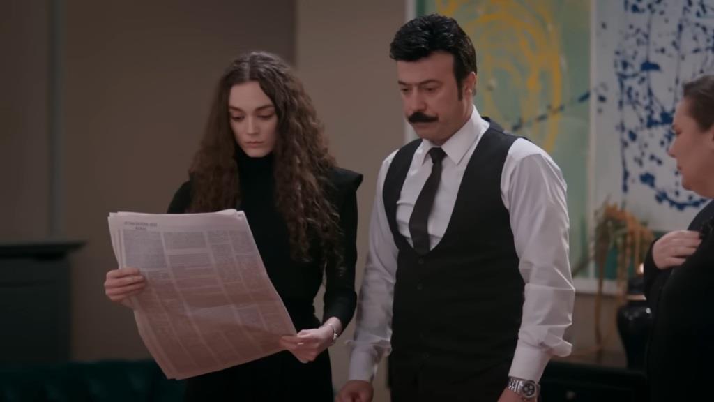 Nana trzyma w rękach gazetę. Obok niej stoi Cenger.