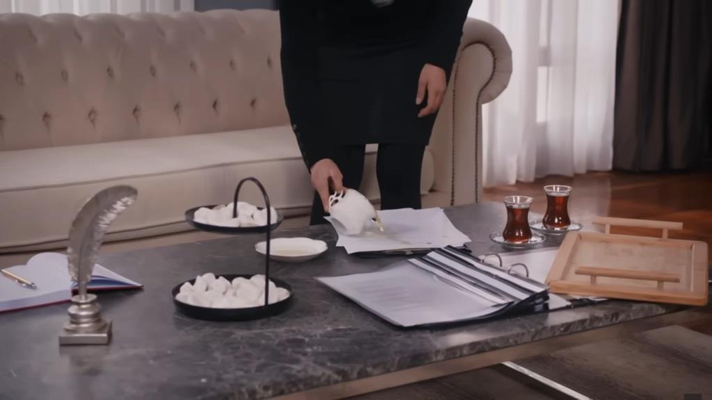 Aynur wylewa herbatę na dokumenty.