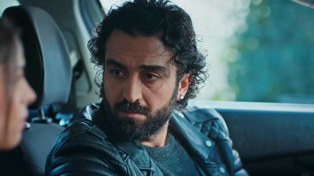 Ferit siedzi za kierownicą. Patrzy na siedzącą na fotelu pasażera Ayse.
