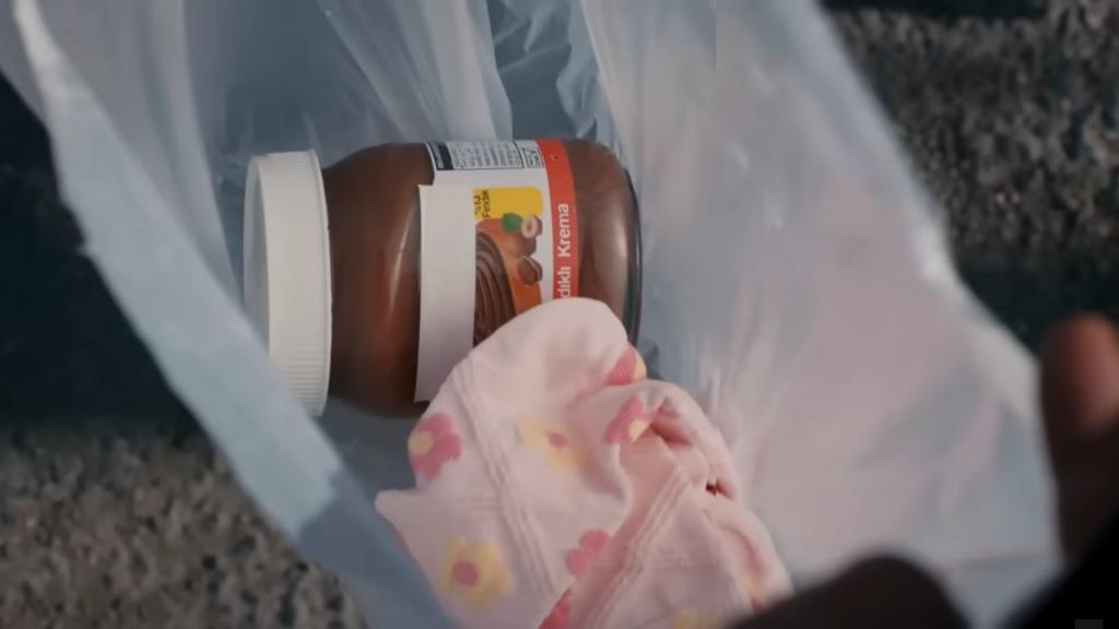 Zbliżenie kamery na produkty w reklamówce - słoik kremu czekoladowego oraz dziecięcą piżamę.