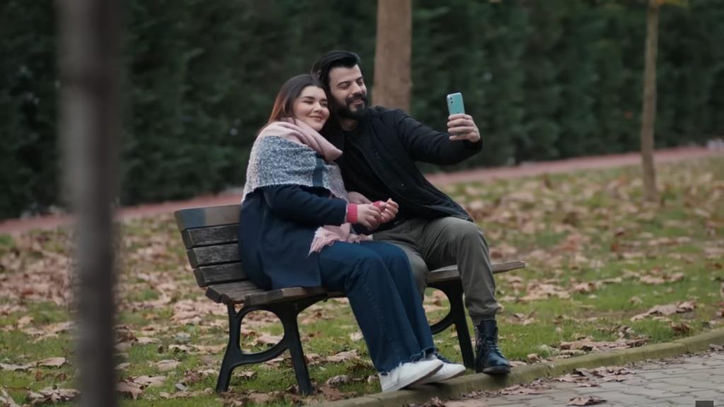 Volkan i Nese siedzą na ławce w parku i robią sobie selfie.
