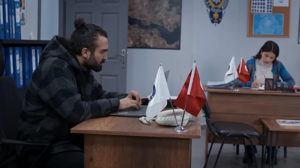 Ferit dyskretnie spogląda na Ayse, siedzącą przy swoim biurku.