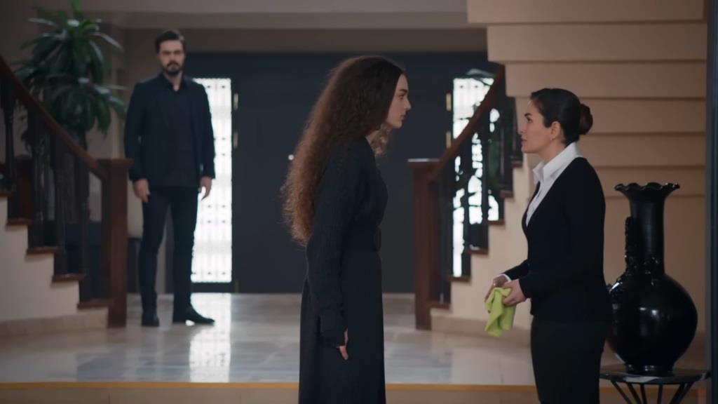 Nana konfrontuje się z Aynur w wejściu do salonu, co Yaman obserwuje, stojąc przy schodach.