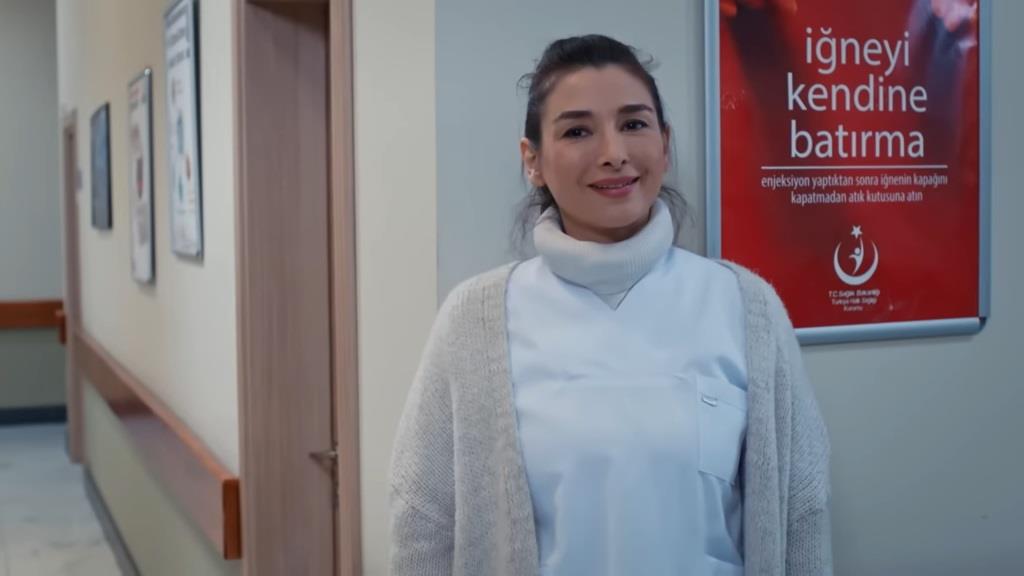 Pielęgniarka Simay. Jest uśmiechnięta i opiera się o ścianę na korytarzu w szpitalu. To ona podrzuciła strzykawkę do marynarki ochroniarza.