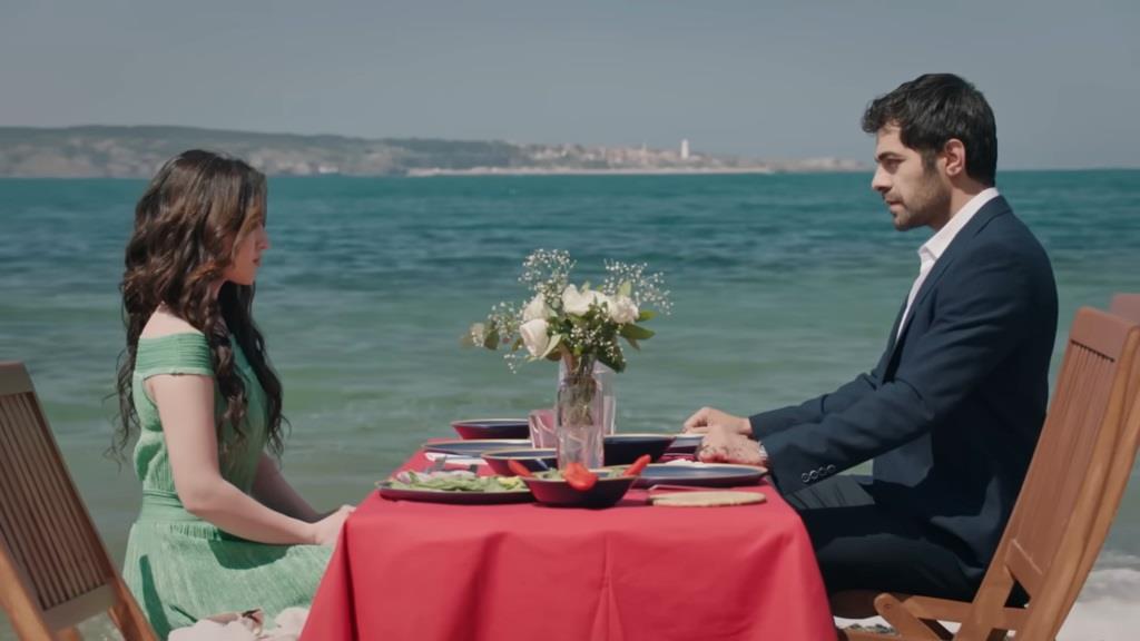 Halil i Zeynep siedzą przy stoliku na plaży.
