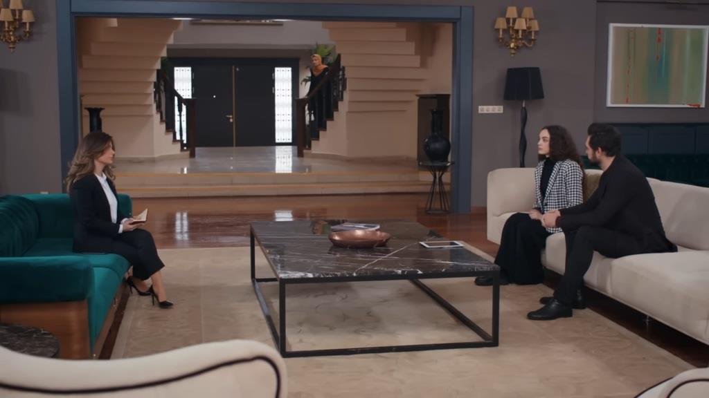 Yaman, Nana i urzędniczka siedzą w salonie. W tle widać stojącą na schodach Akcę.