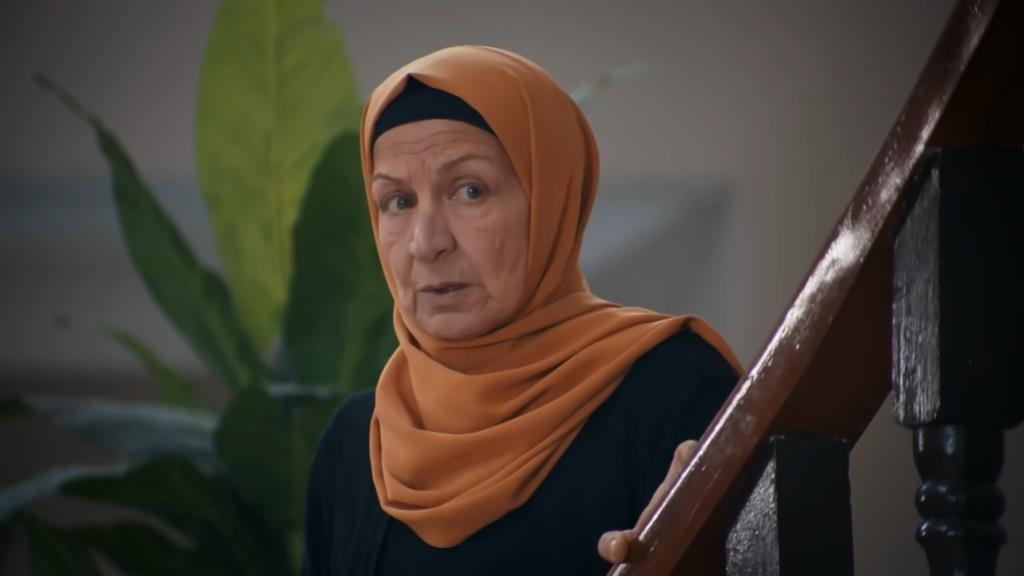 Akca stoi na schodach, skąd obserwuje rozmowę w salonie.