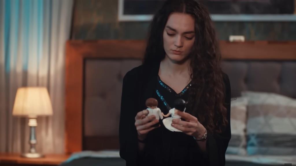 Nana siedzi na łóżku. W rękach trzyma figurki z tortu ślubnego.