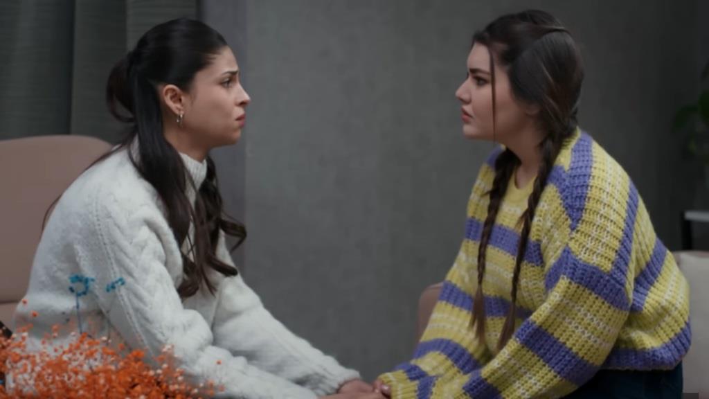 Ayse i Nese siedzą naprzeciwko siebie i trzymają się za ręce. Ich spojrzenia są pełne emocji.