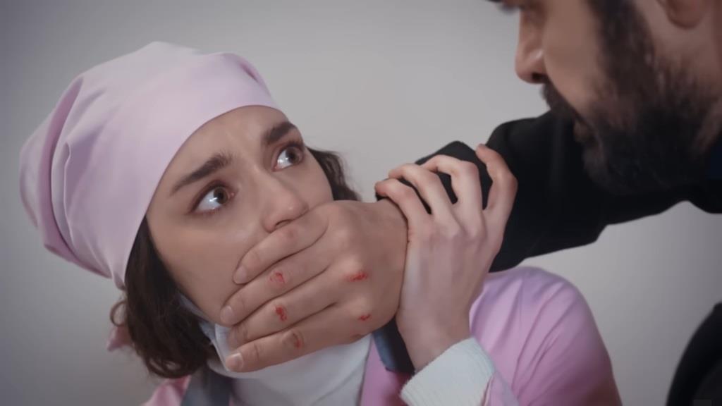 Nana w przebraniu salowej. Yaman zakrywa jej usta dłonią.