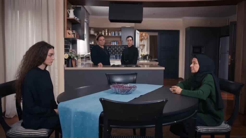 Scena w kuchni. Nana i Akca siedzą naprzeciwko siebie przy stole.