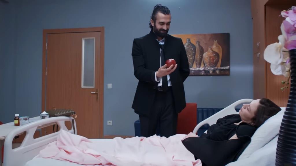 Ferit stoi przed Akasyą, trzymając w ręku czerwone jabłko.