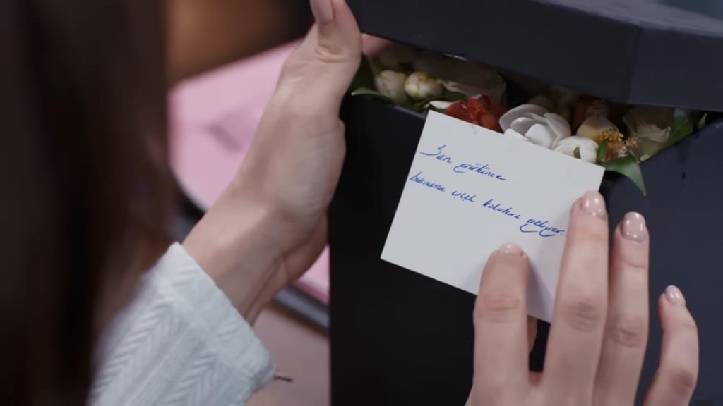 Zbliżenie na znajdujące się w pudełku kwiaty oraz liścik od nadawcy.