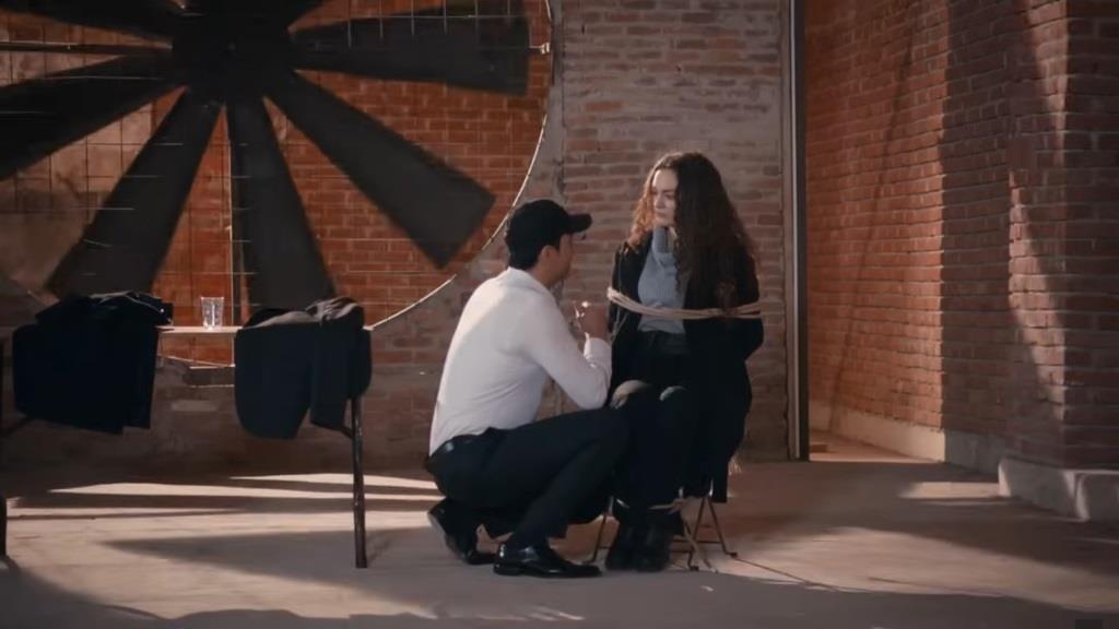 Nedim kuca obok przywiązanej do krzesła Nany.