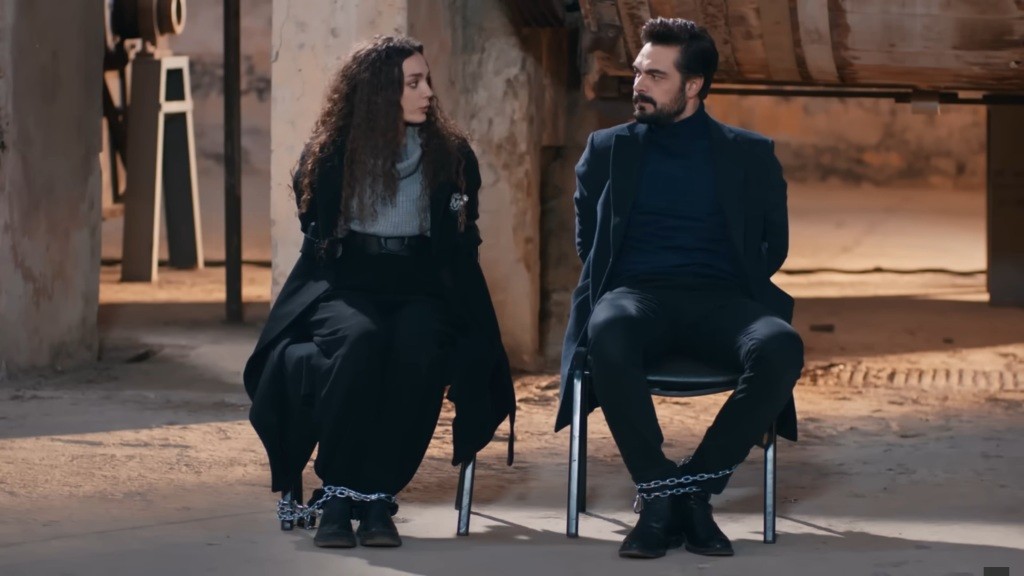 Kadr przedstawia Nanę i Yamana w magazynie. Są przykuci łańcuchami do krzeseł.