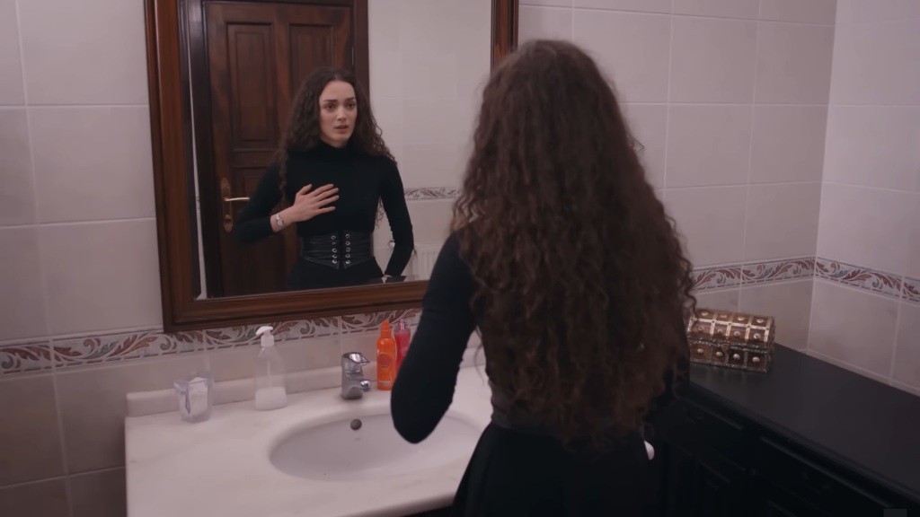 Nana stoi przed lustrem w łazience i trzyma się za serce.