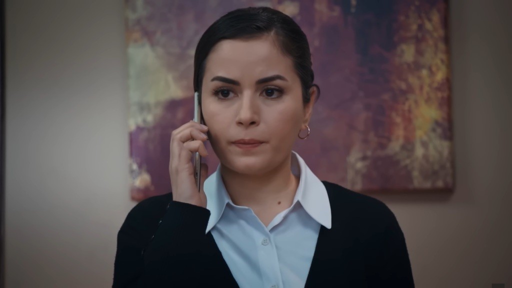 Aynur trzyma telefon przy policzku.