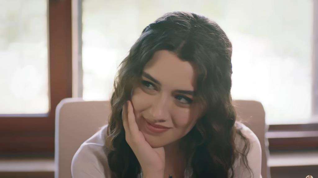 Zeynep uśmiecha się, opierając brodę na dłoni.