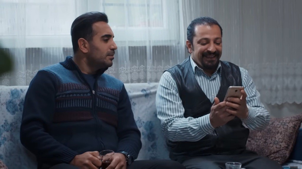 Idris czyta wiadomość od Aynur. Kazim siedzi obok niego.