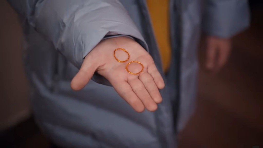 Zbliżenie na dwie złote obrączki spoczywające na dłoni Yusufa.