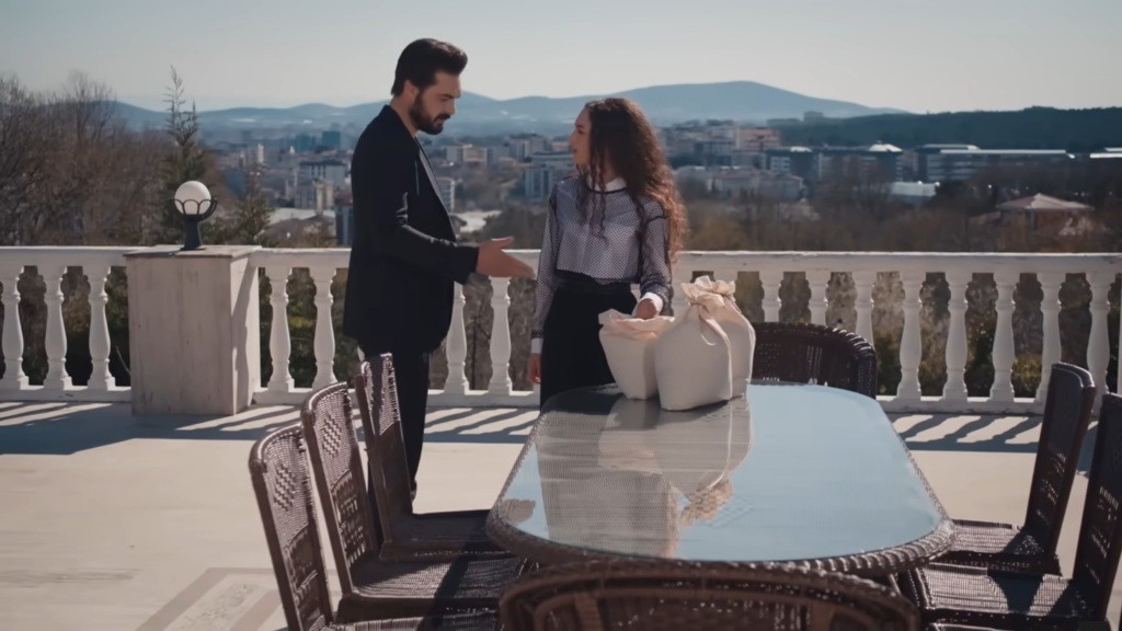 Yaman pokazuje ręką na trzy worki z karmą dla ptaków. Obok stoi Nana.