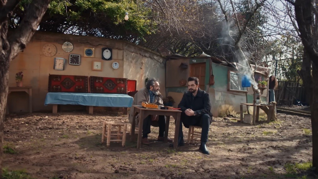 Scena przed chatą Veliego.Yaman i Veli siedzą przy stoliku.