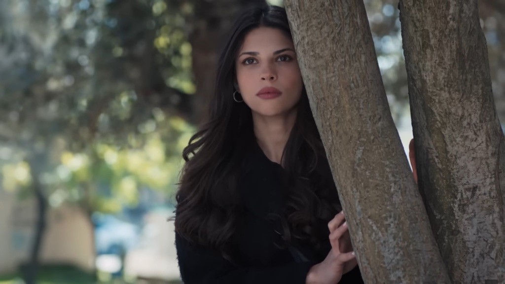 Ayse wygląda zza drzewa.