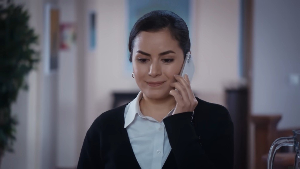 Aynur uśmiecha się, rozmawiając przez telefon.