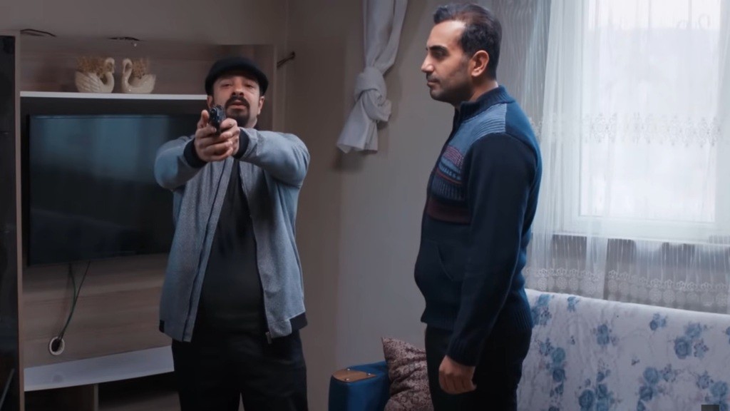 Idris unosi broń. Obok stoi Kazim.