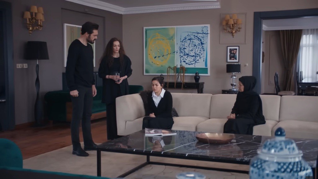 Aynur siedzi na kanapie w salonie rezydencji. Obok niej znajdują się Yaman, Nana i Akca.