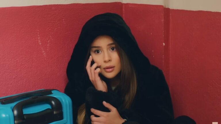 Elif rozmawia przez telefon, kuląc się w kącie.