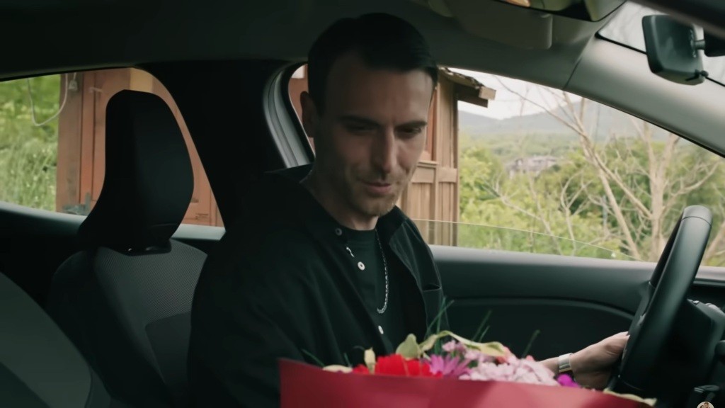 Alper siedzi w samochodzie i patrzy na bukiet kwiatów.
