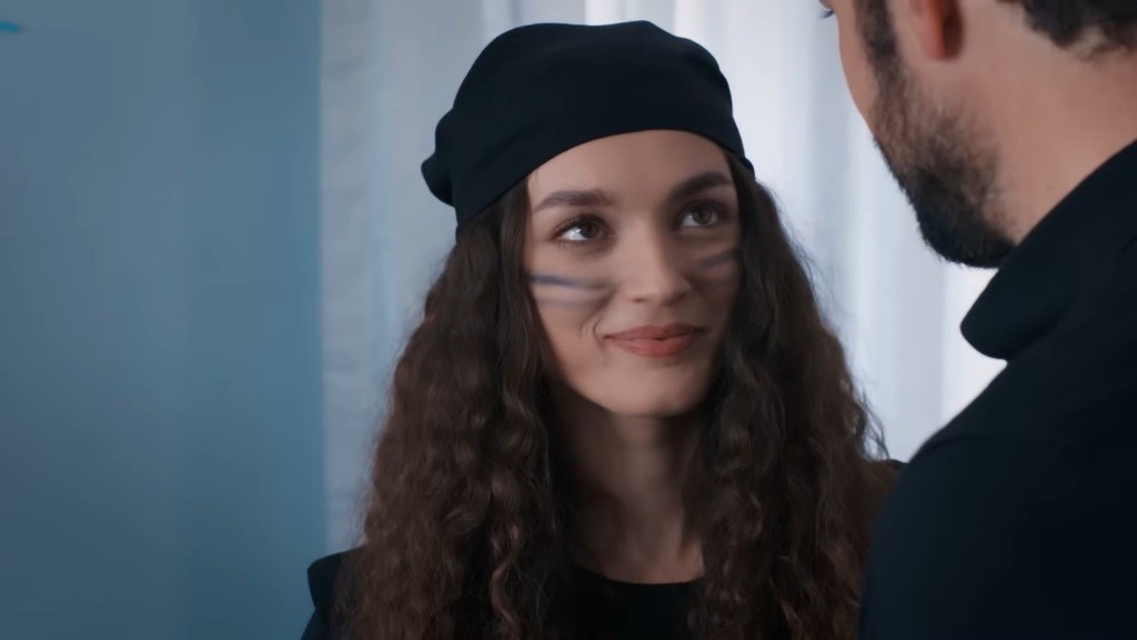 Nana ma pomalowane policzki i czarną bandanę na głowie. Uśmiecha się, patrząc na Yamana.